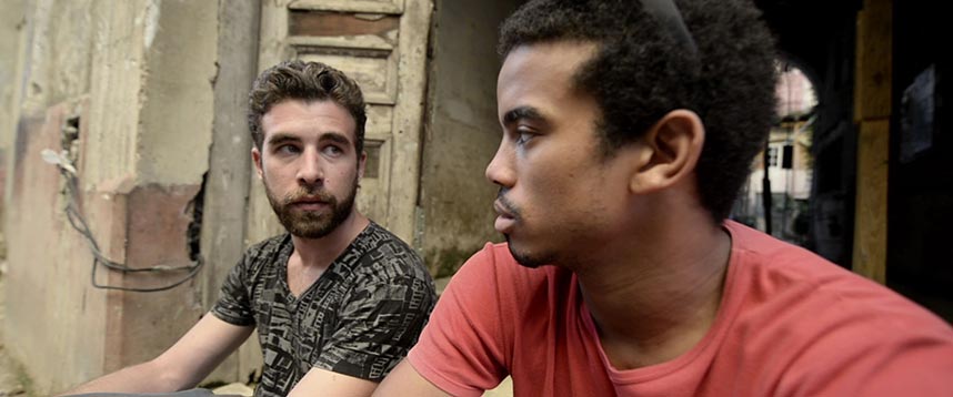 Two men stare at each other against the background of a worn Cuban building