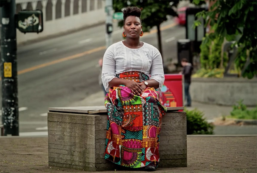 A woman in a colorful skirt sits beside an intersection.